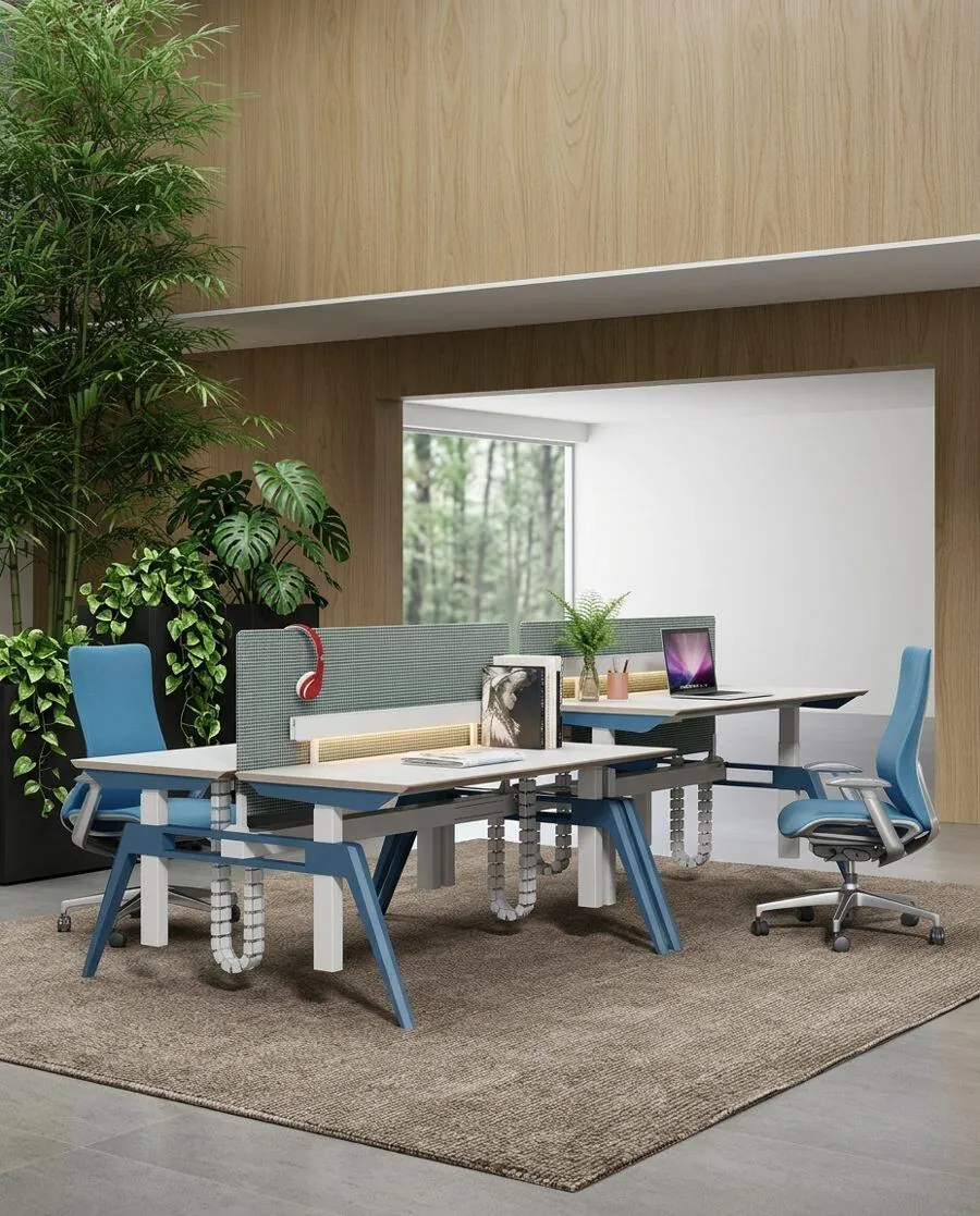 Estaciones de trabajo corporativas bench con sillas ergonómicas azules, paneles acústicos y plantas integradas frente a ventanal con vista al bosque