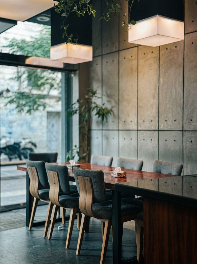 Comedor contemporáneo para restaurante con mesa de nogal, sillas tapizadas grises y muro de concreto aparente
