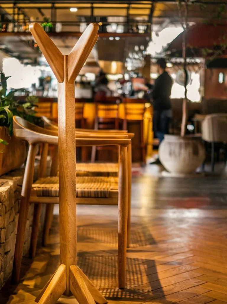 Interior de restaurante con perchero escultórico de madera, sillas de asiento tejido y piso de parquet